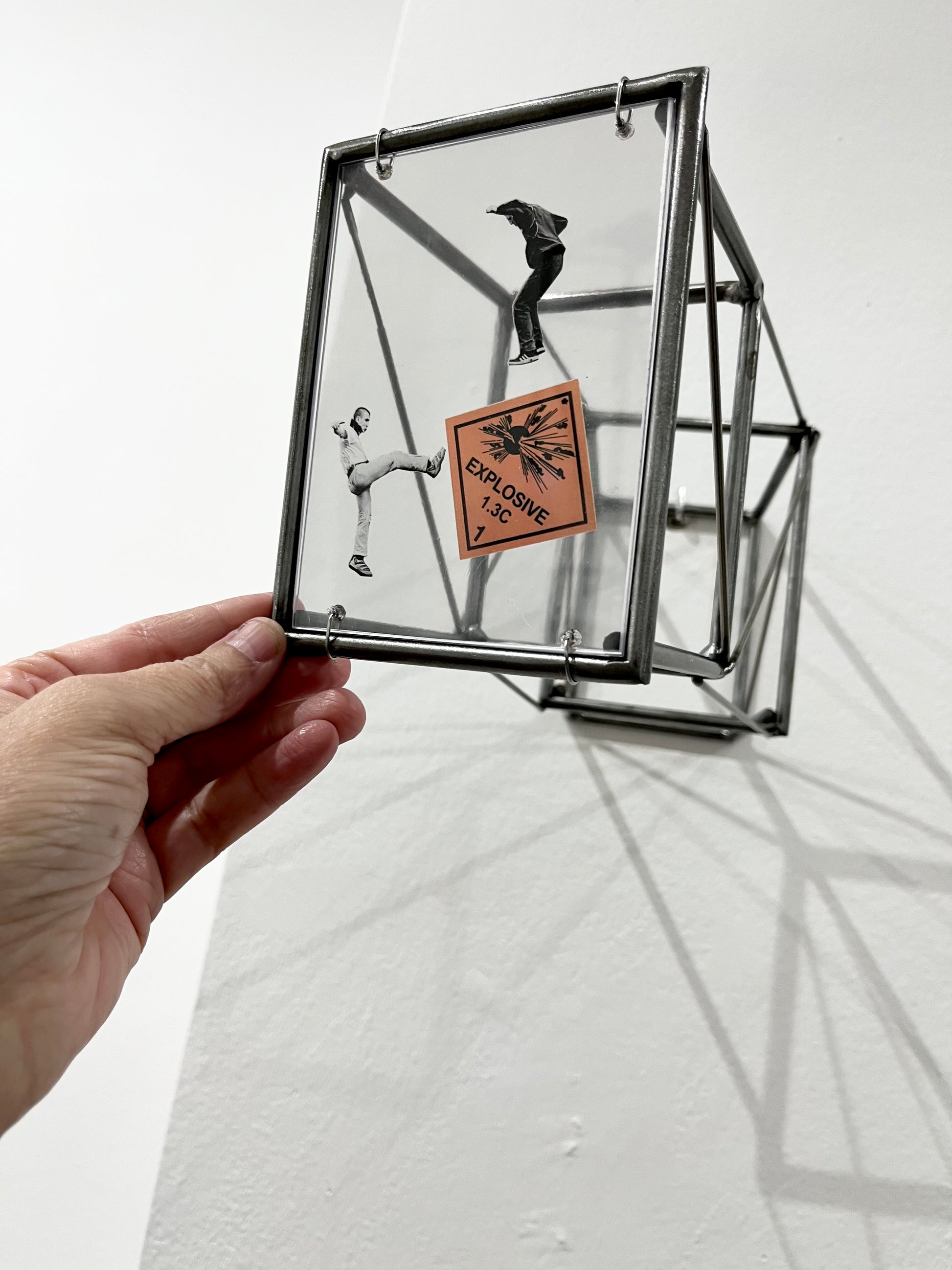 # human hand touching frame of steel wall sculpture with surrealist collage of human figures in action. Numbered Limited Edition Wall Sculpture Social Explosion Sign: Limited Edition Light and Shadow Sculpture Artandshadow