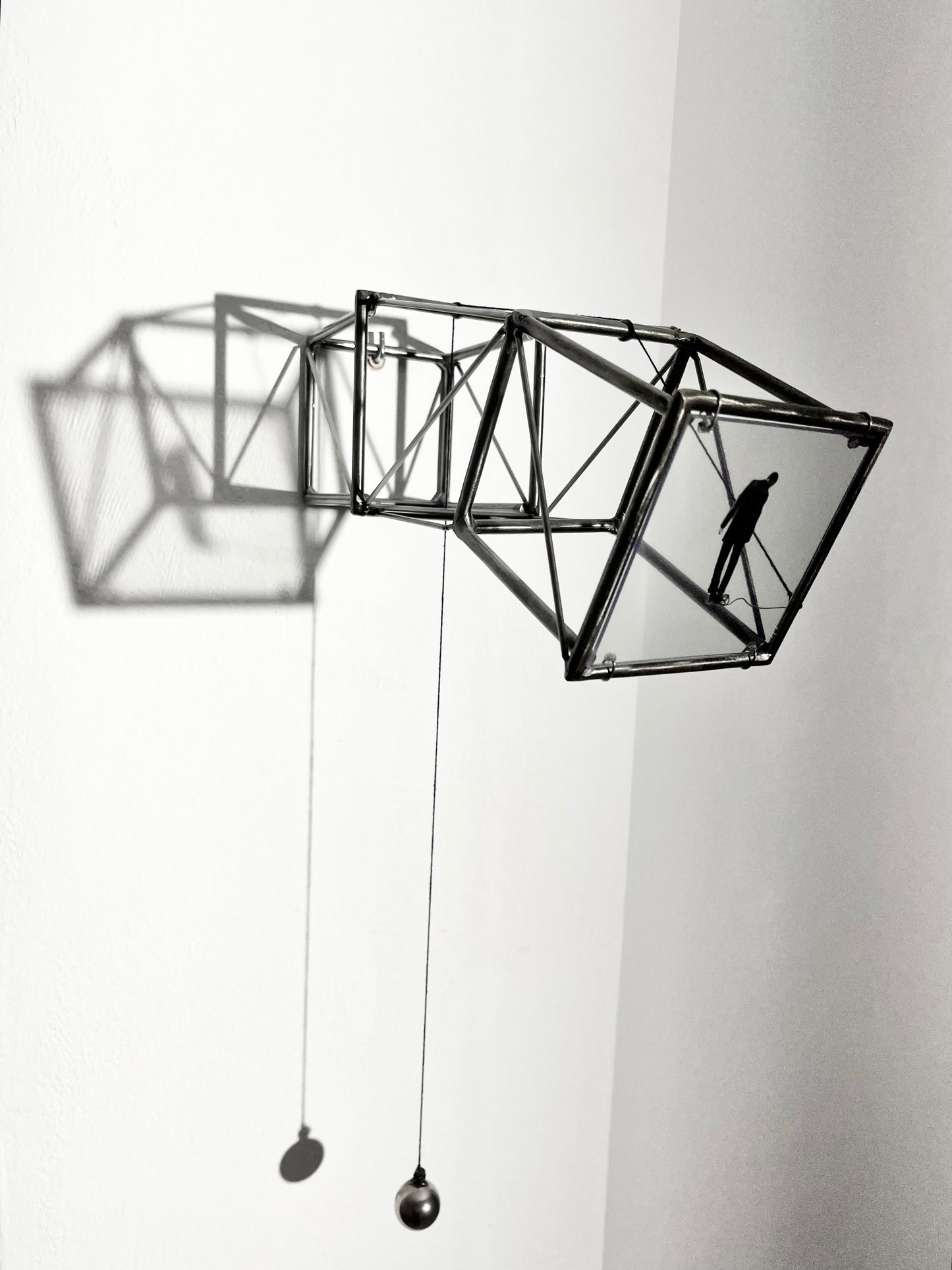 Hanging by a Thread is stylish, contemporary light and shadow sculpture, a geometric form given an asymetric twist, designed to lend any interior a quirky modernist elegance. An steel shadow artpiece depicting a man looking at his foot caught up in a thread leading to a stainless steel pendulum ball woven into the handmade structure. The image is a high quality print of an original Furst_Ori collage designed to caste a shadow within the frame.