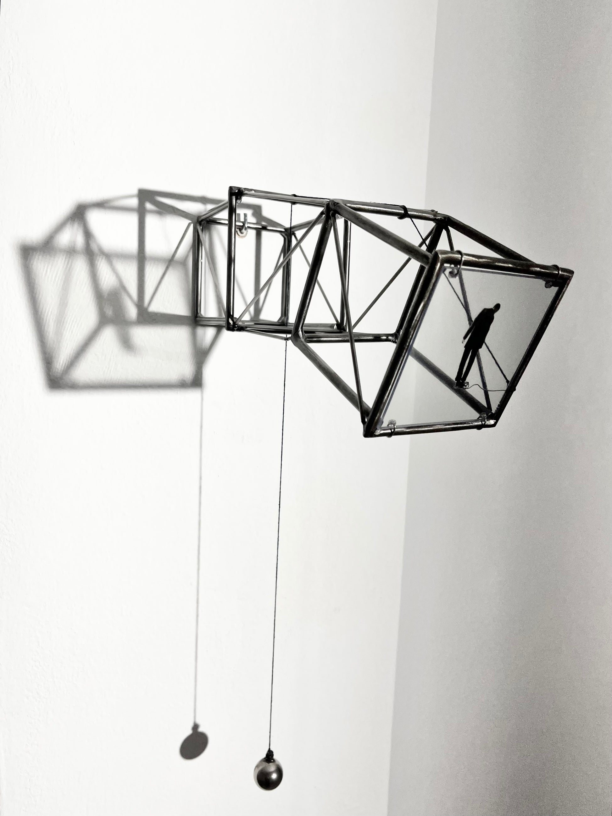 Hanging by a Thread is stylish, contemporary light and shadow sculpture, a geometric form given an asymetric twist, designed to lend any interior a quirky modernist elegance. An steel shadow artpiece depicting a man looking at his foot caught up in a thread leading to a stainless steel pendulum ball woven into the handmade structure. The image is a high quality print of an original Furst_Ori collage designed to caste a shadow within the frame.