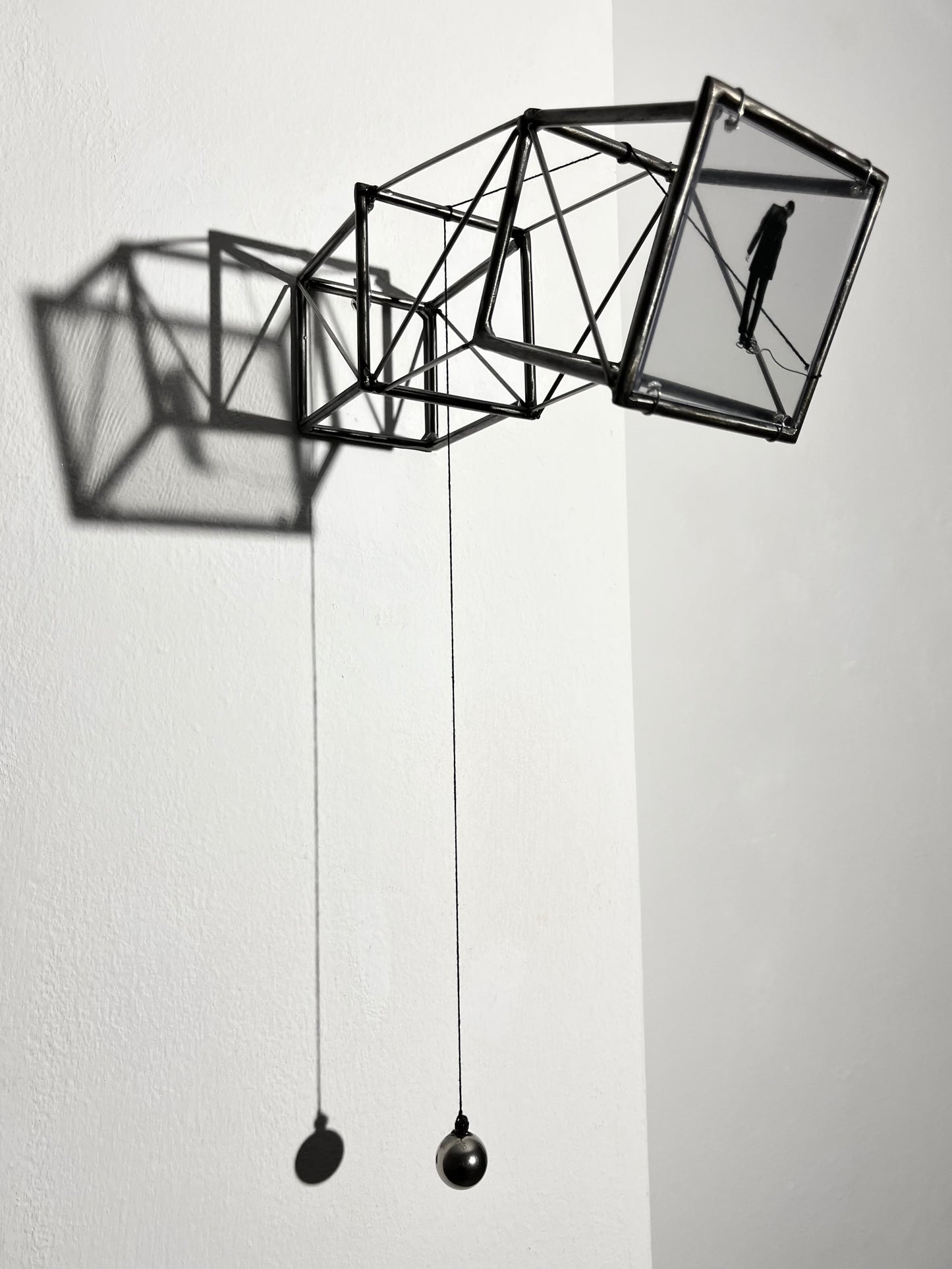 Hanging by a Thread is stylish, contemporary light and shadow sculpture, a geometric form given an asymetric twist, designed to lend any interior a quirky modernist elegance. An steel shadow artpiece depicting a man looking at his foot caught up in a thread leading to a stainless steel pendulum ball woven into the handmade structure. The image is a high quality print of an original Furst_Ori collage designed to caste a shadow within the frame.