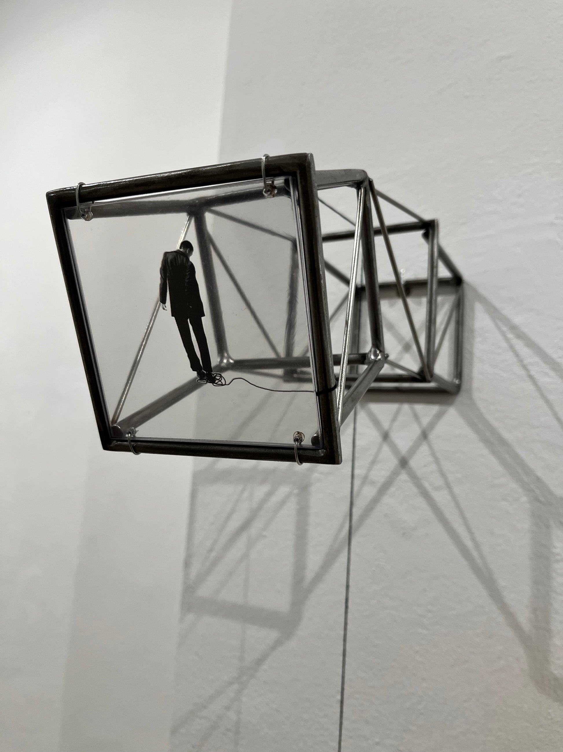 Hanging by a Thread is stylish, contemporary light and shadow sculpture, a geometric form given an asymetric twist, designed to lend any interior a quirky modernist elegance. An steel shadow artpiece depicting a man looking at his foot caught up in a thread leading to a stainless steel pendulum ball woven into the handmade structure. The image is a high quality print of an original Furst_Ori collage designed to caste a shadow within the frame.