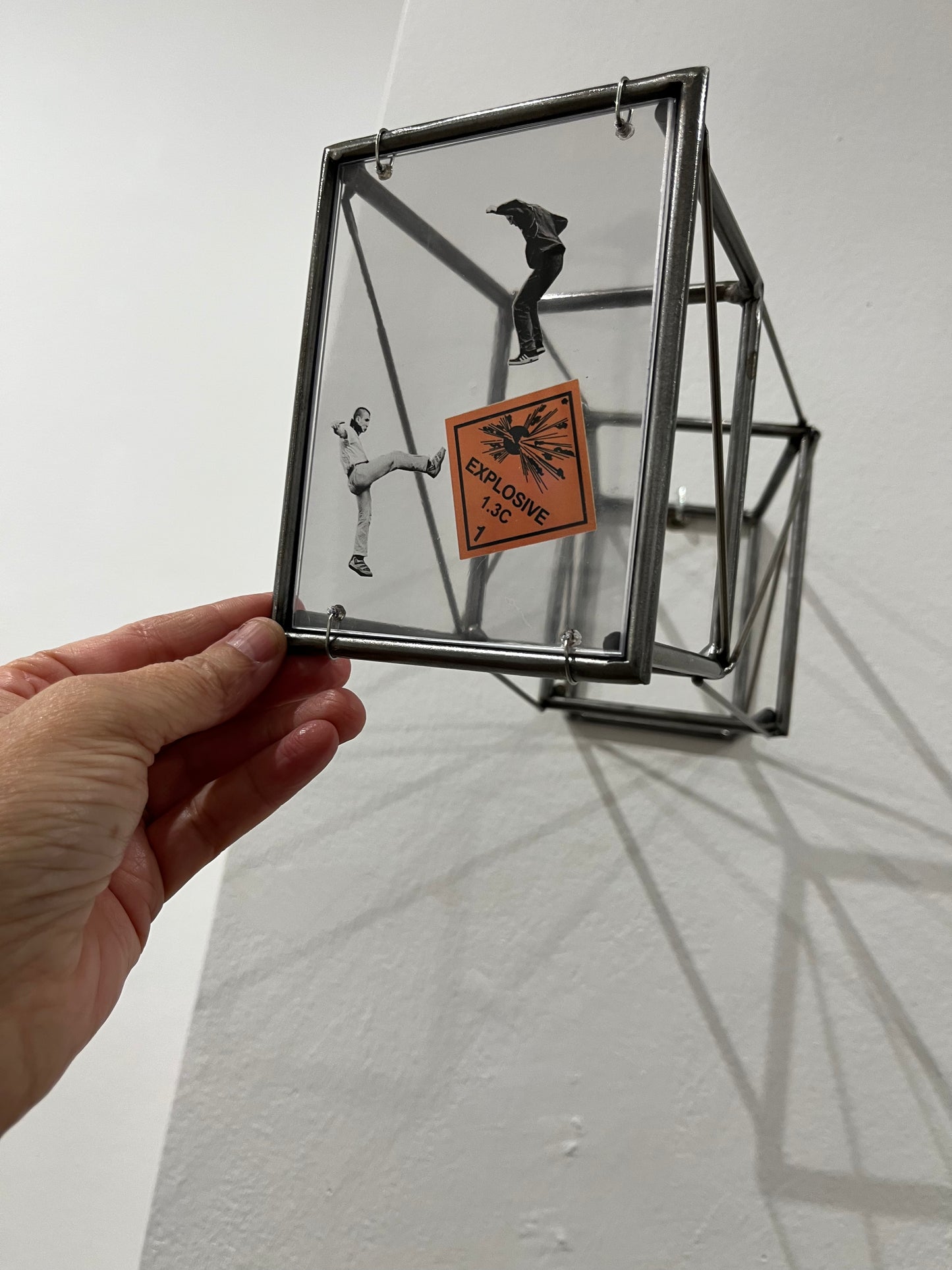 Hand holding a glass box with a silhouette of a person and an 'explosive' label on a white background