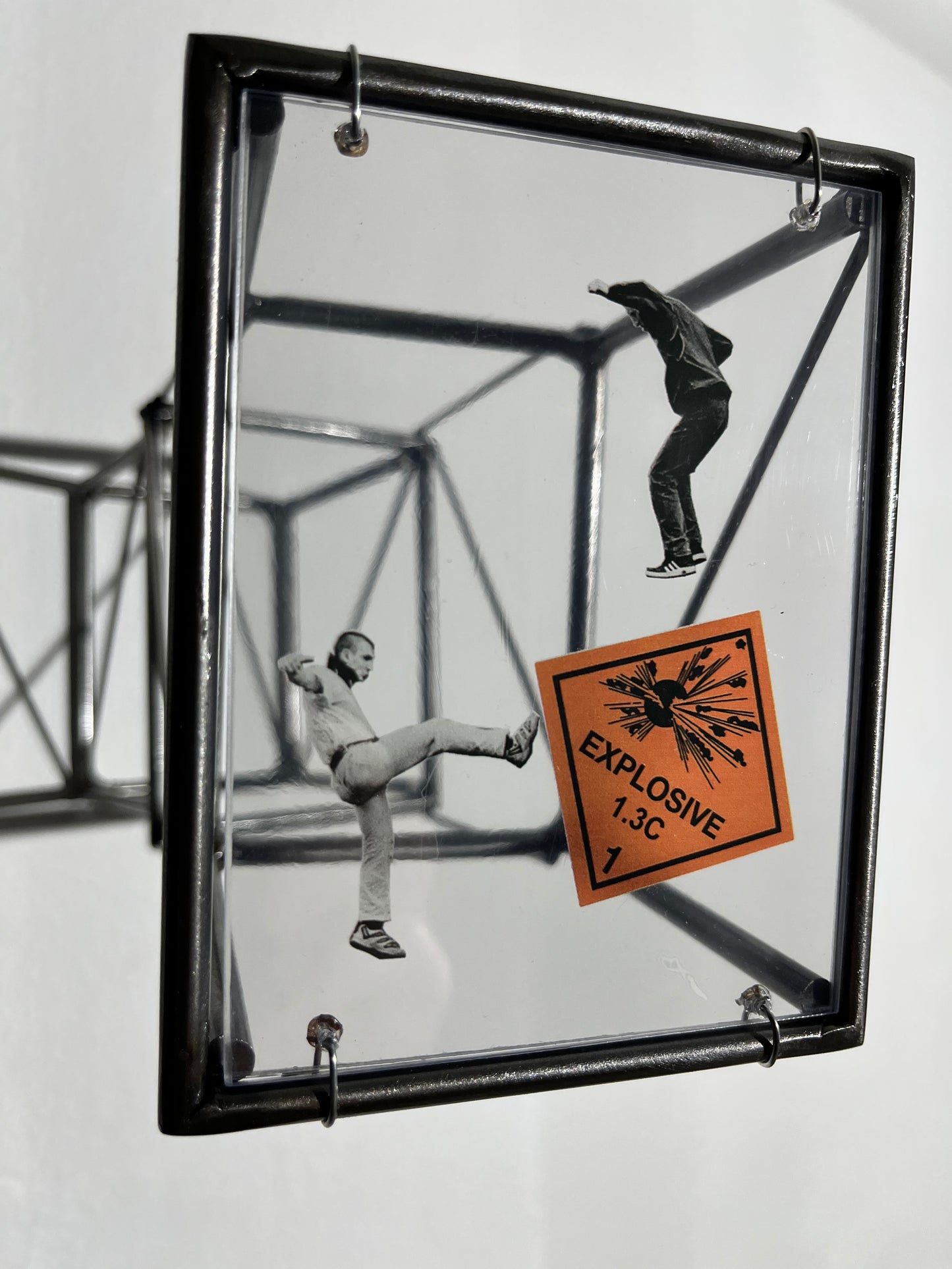 Glass panel with black metal frame showing two figures and an 'Explosive' label.