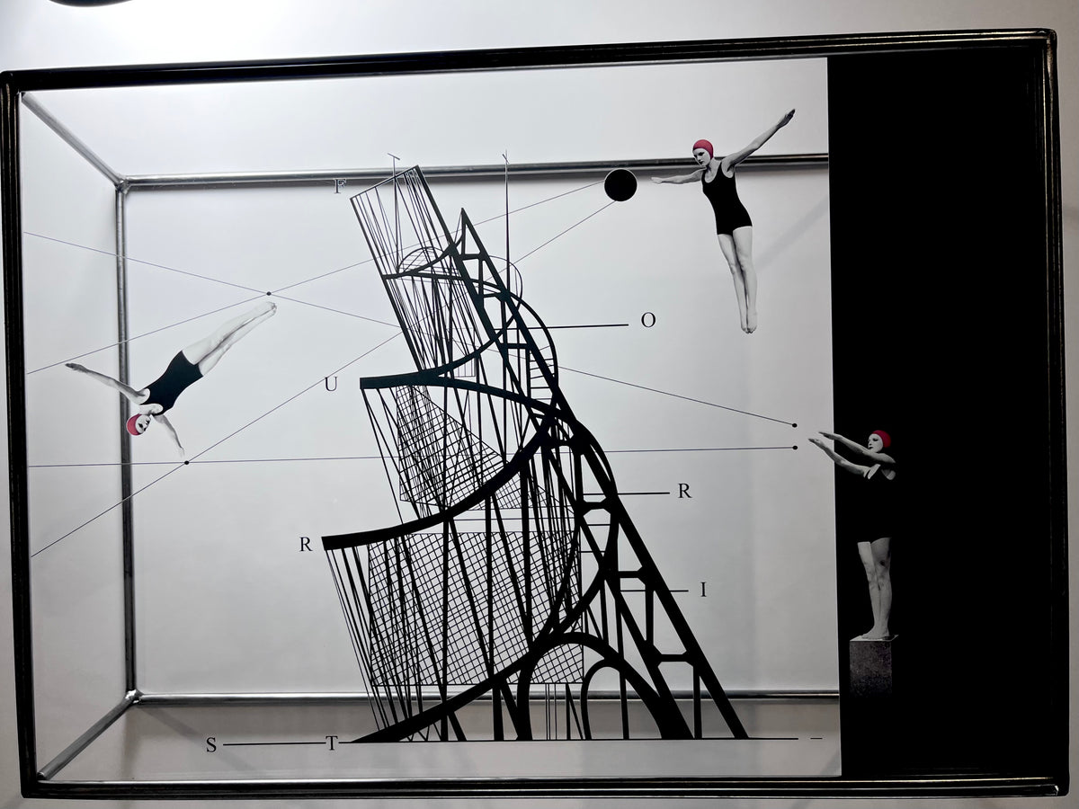 A framed black and white art print featuring a surreal composition with three figures in leotards, a large abstract geometric structure, and measurement-like labels, shown in a square frame against a light wall.